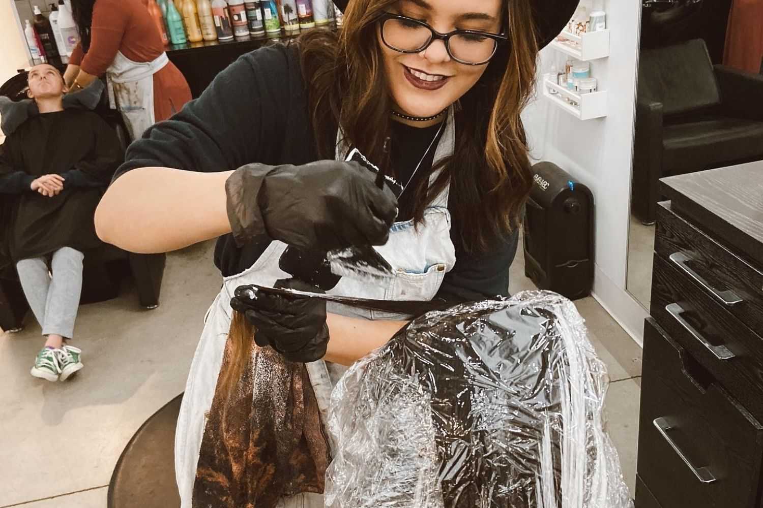Hairdresser dyes hair with plastic wrap at salon.