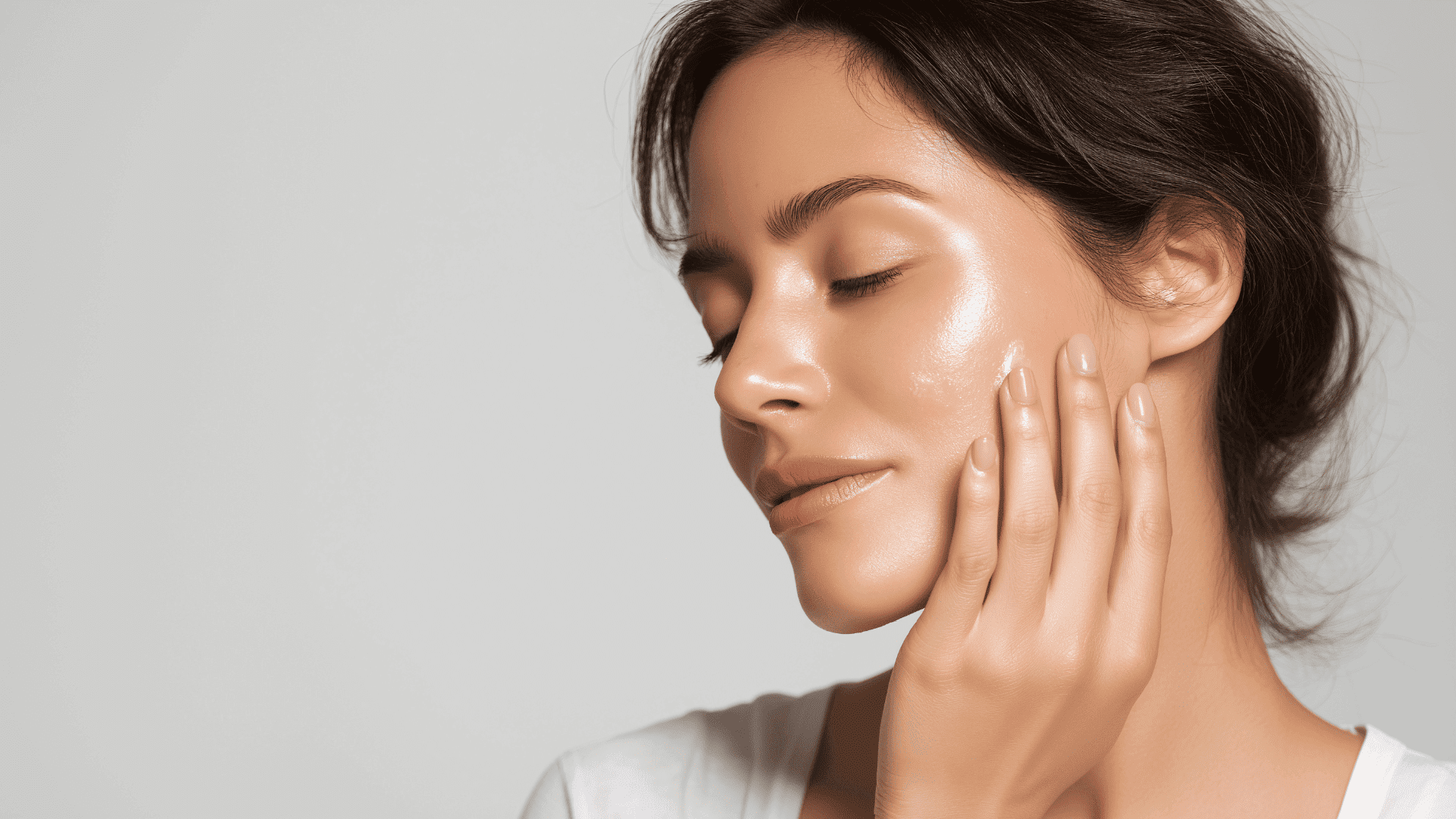 A serene woman with glowing skin touching her cheek, eyes closed.