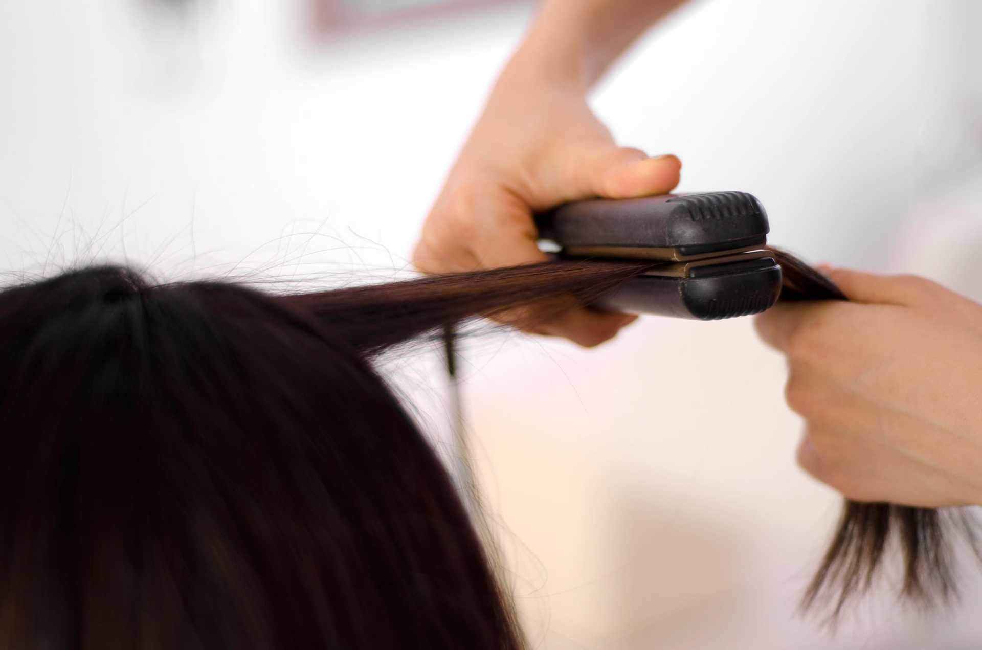 Hair being straightened with a flat iron, close-up view.
