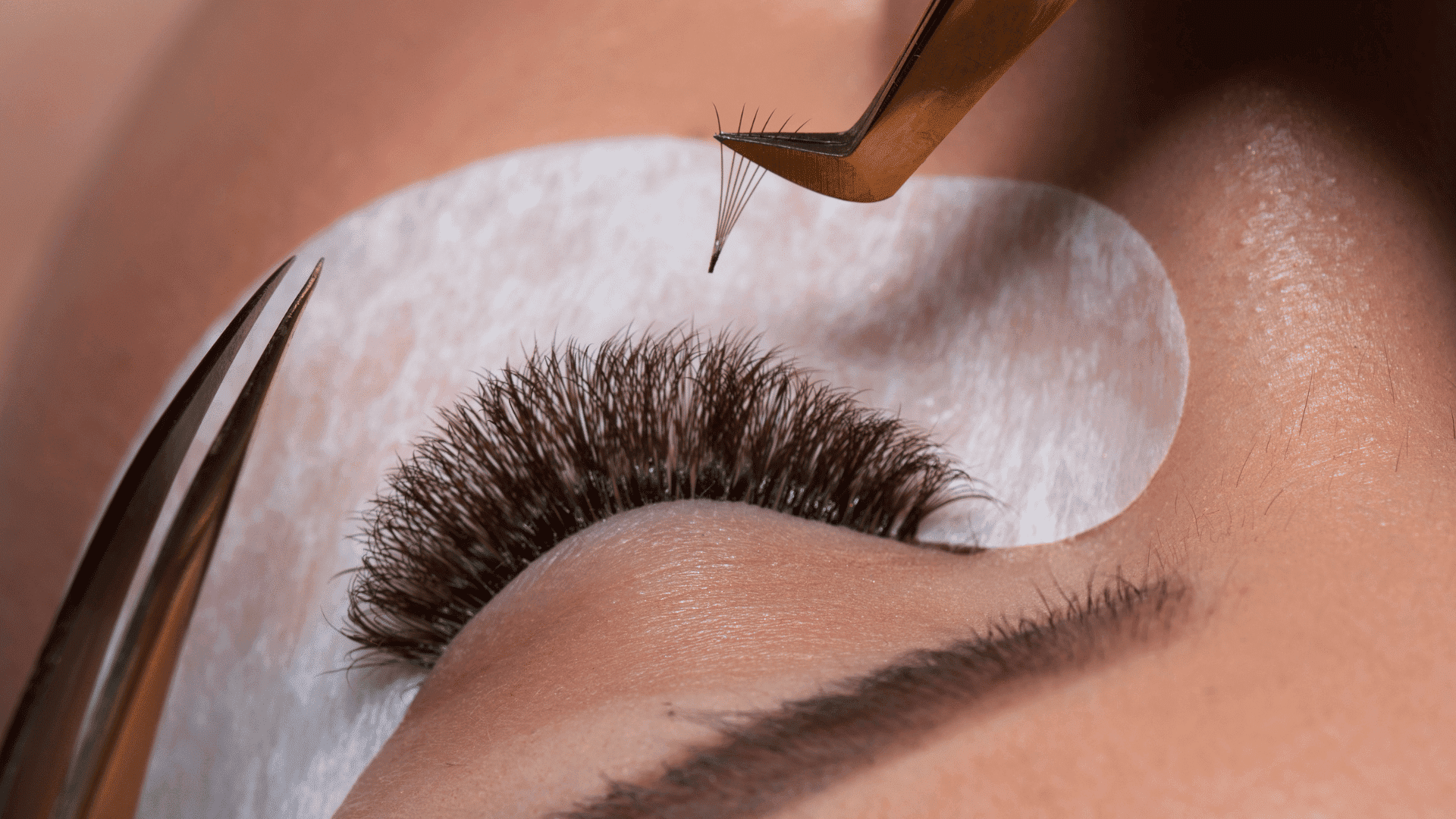 Eyelash extension procedure with tweezers and pad on a person's closed eye.