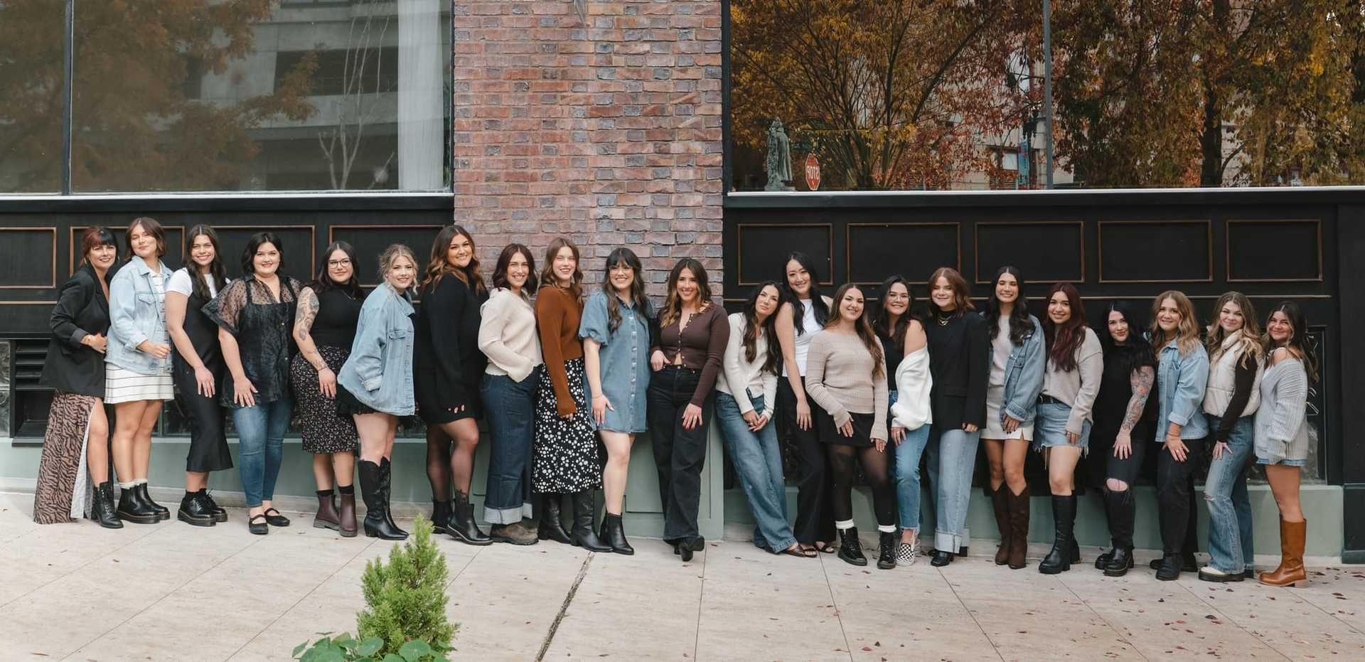 A group of people posing together in casual attire against a brick wall backdrop.