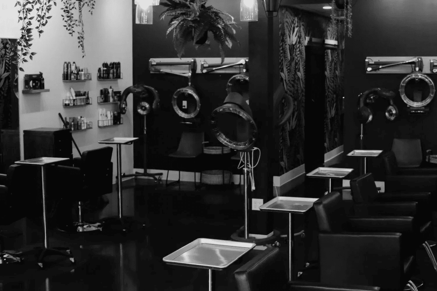 Modern hair salon with styling stations and hair dryers, decorated with plants and dark colors.