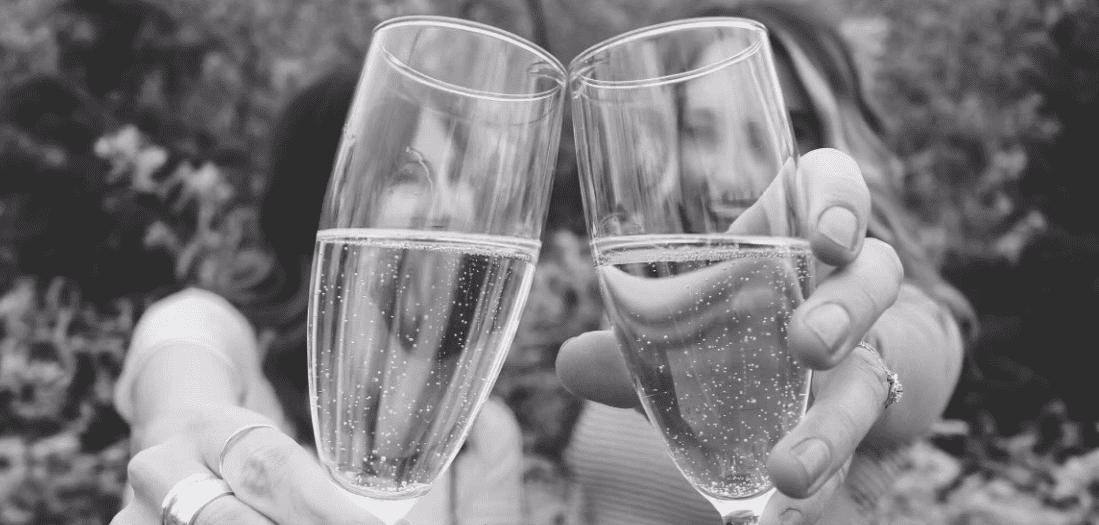 Two people clinking champagne glasses in a celebratory toast, with a blurred background.