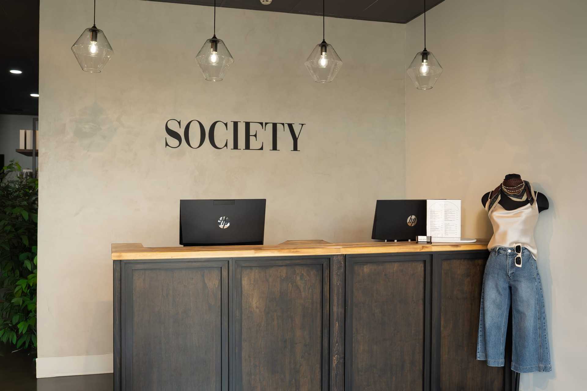 Reception desk with two laptops, mannequin in jeans, and pendant lights in a stylish interior.