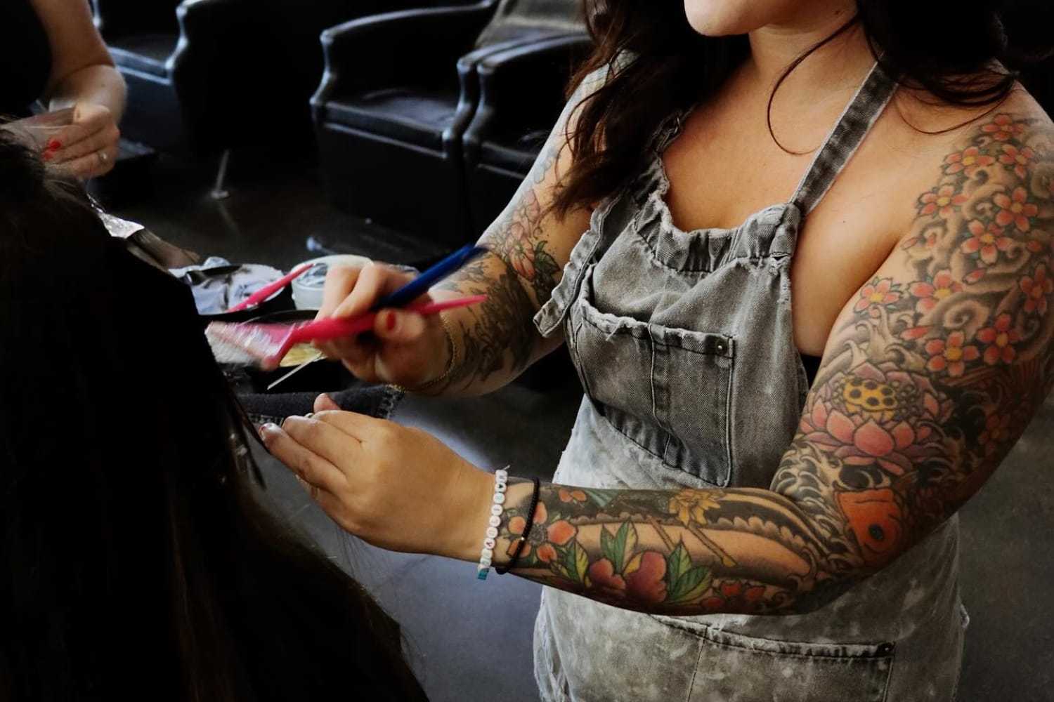 Tattooed stylist coloring hair in a salon setting.