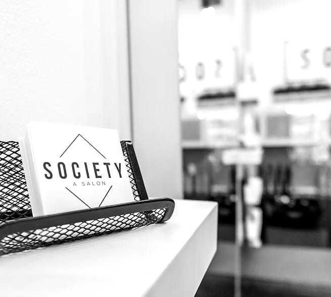 Salon reception counter with "Society: A Salon" card in holder, blurred background.