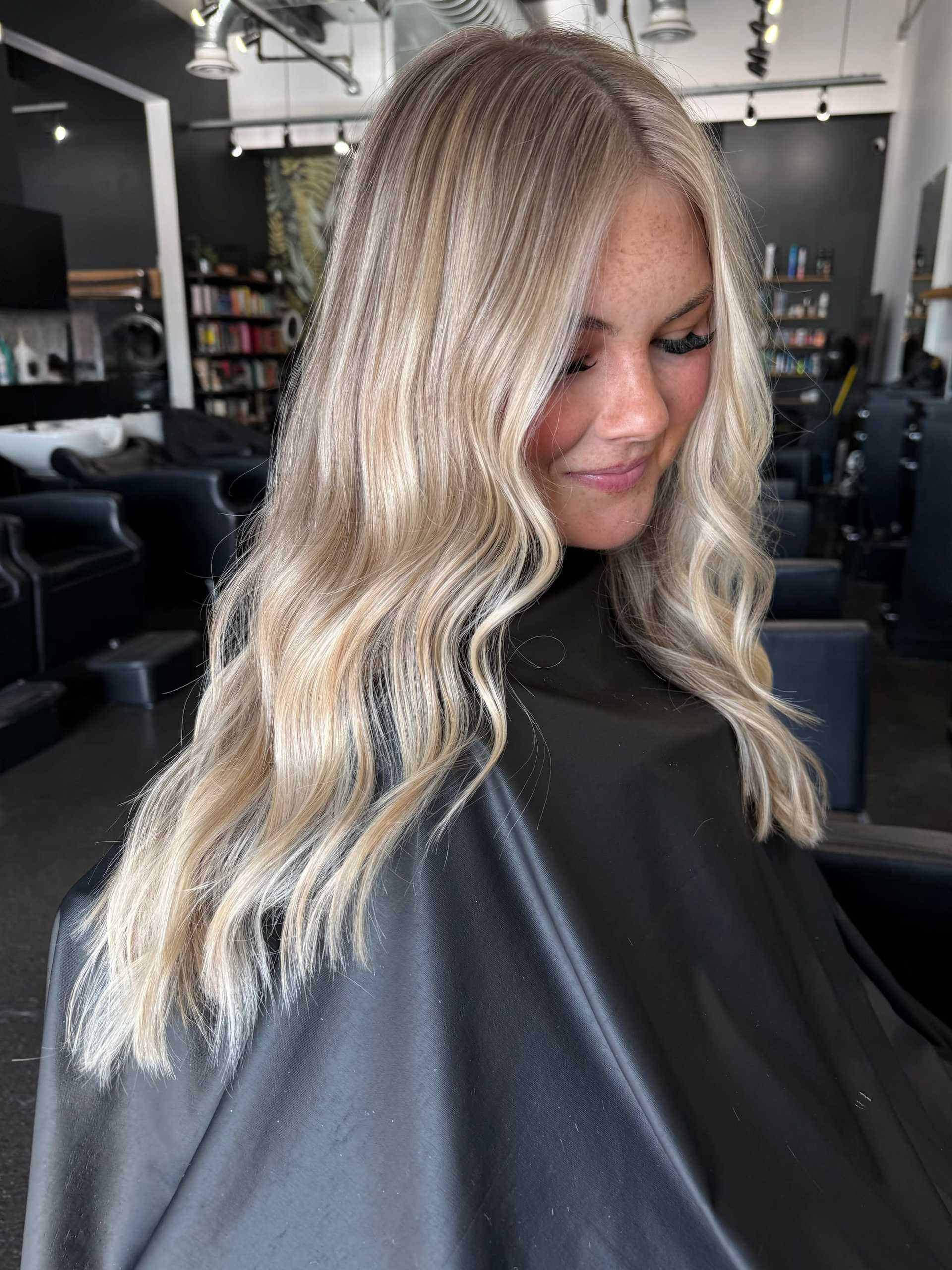 Blonde woman with wavy hair smiling in a modern hair salon.