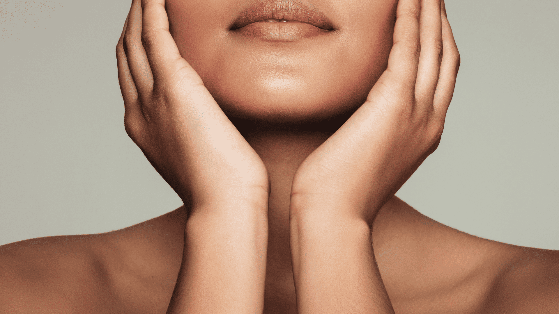 Hands gently touching a face with smooth skin and neutral background.